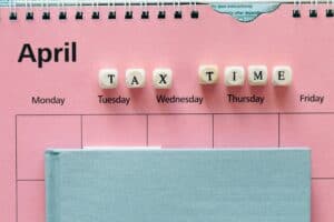 A notebook on a pink calendar, and dice that spell out TAX TIME