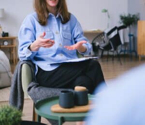 A businesswoman with notes and a pen sitting at a coffee table explaining something.