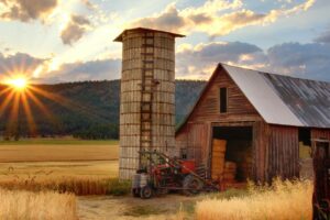A farm shed with sun setting and hills in the background.